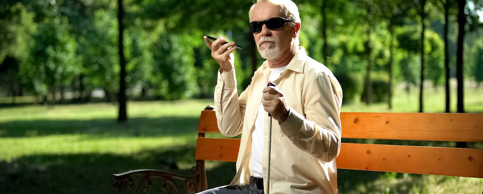 Blind man sitting on a park bench listening to his phone