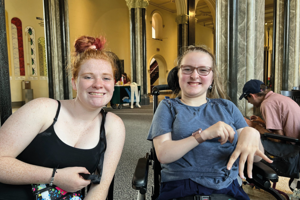 Two young women sitting next to each other, one in a wheelchair.