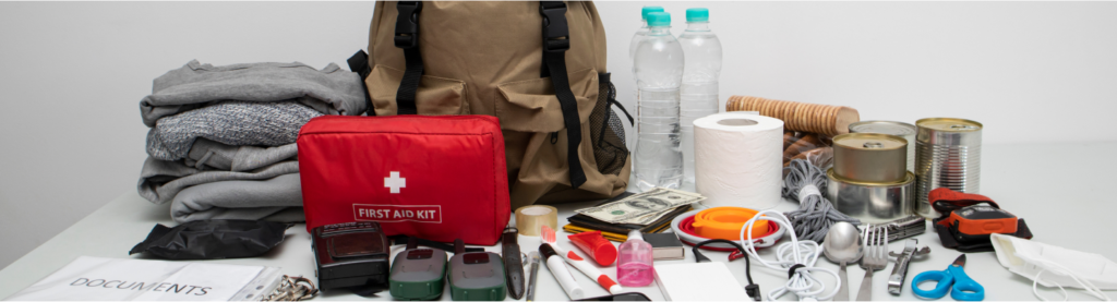 Elementos que deben ir en una bolsa de emergencia, como un botiquín de primeros auxilios, mantas, dinero en efectivo, cubiertos, papel higiénico, comida enlatada y tijeras.