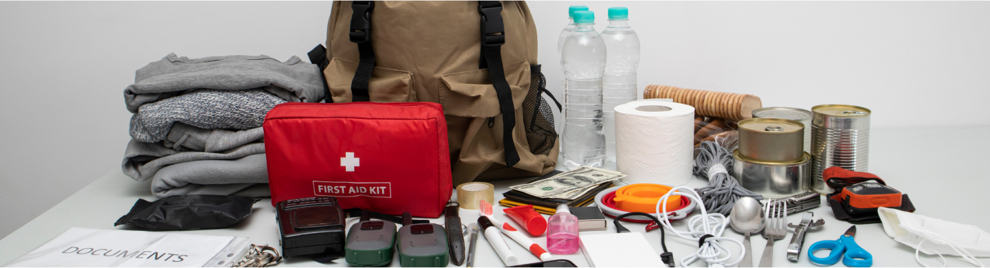 Elements that go into an emergency go bag, including a first aid kit, blankets, cash, cutllery, toilet paper, canned food and scissors.