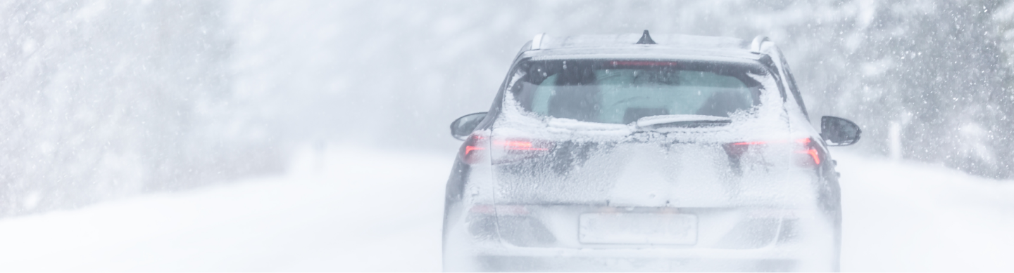 Car driving down a street in a massive snowstorm.