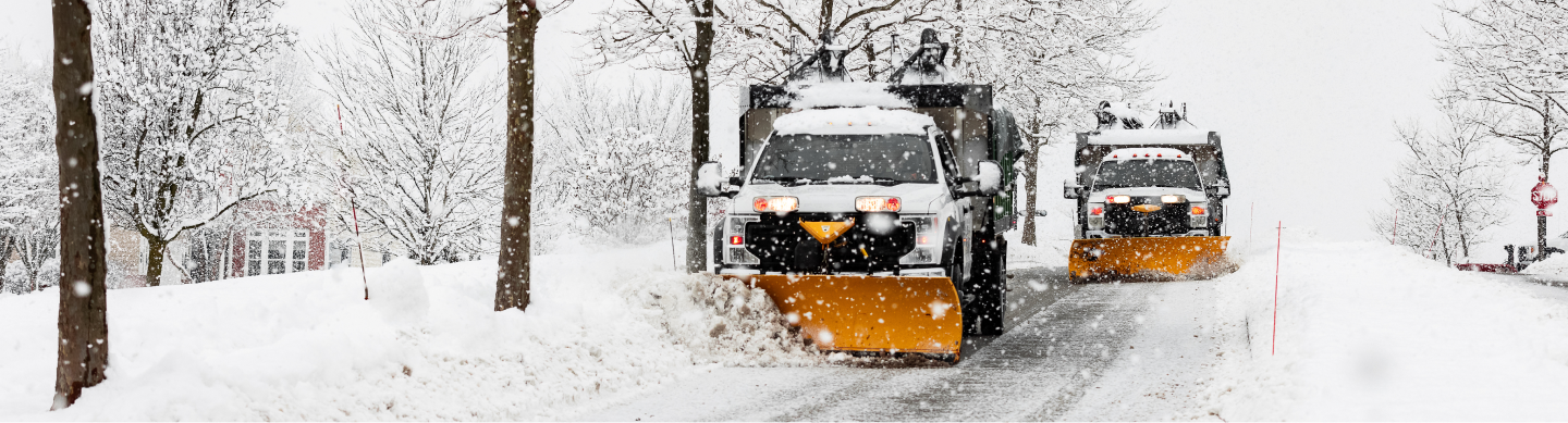 Two snowplows going down a residential street in a massive snowstorm.